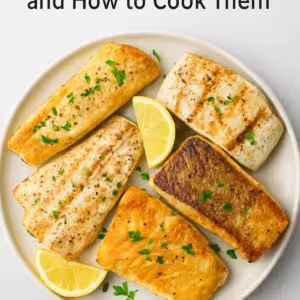 Cooked white fish fillets on a plate, including cod, tilapia, and halibut, garnished with lemon and parsley